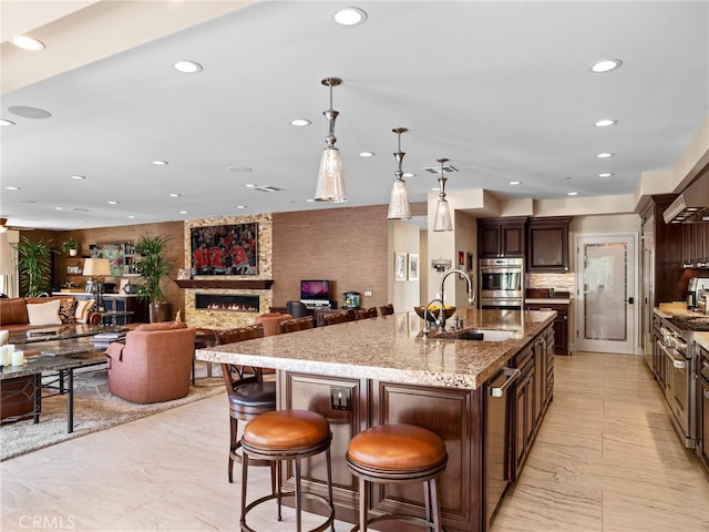 kitchen featuring a large island with sink, a breakfast bar, pendant lighting, dark brown cabinets, and sink