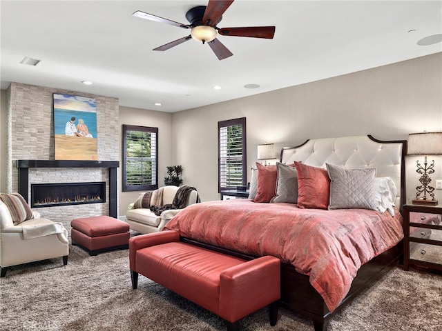 bedroom with ceiling fan, a stone fireplace, and carpet flooring