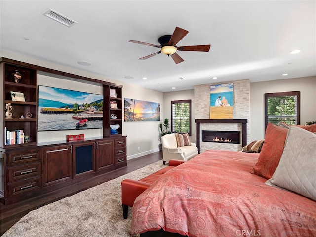 bedroom featuring a large fireplace, multiple windows, dark hardwood / wood-style floors, and ceiling fan