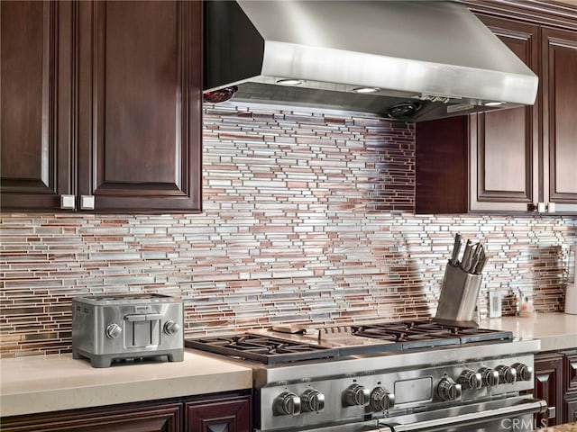 kitchen with decorative backsplash, stainless steel stove, dark brown cabinets, and wall chimney range hood