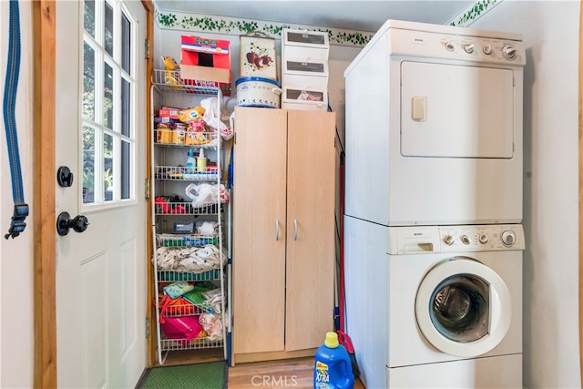 clothes washing area featuring stacked washer / drying machine, wood-type flooring, and cabinets