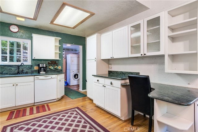 kitchen featuring sink, white cabinetry, dishwasher, light wood-type flooring, and stacked washer / drying machine