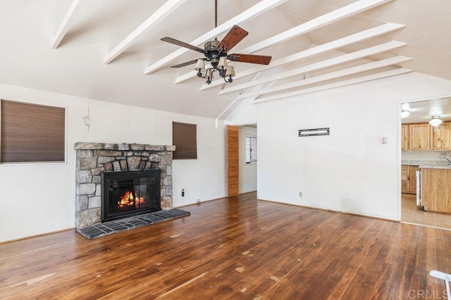 living room with vaulted ceiling with beams, ceiling fan, hardwood / wood-style floors, and a stone fireplace