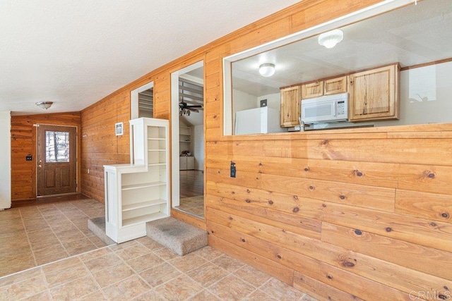 interior space with ceiling fan, light brown cabinets, and wood walls