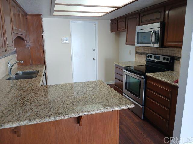 kitchen featuring kitchen peninsula, sink, appliances with stainless steel finishes, dark hardwood / wood-style flooring, and decorative backsplash