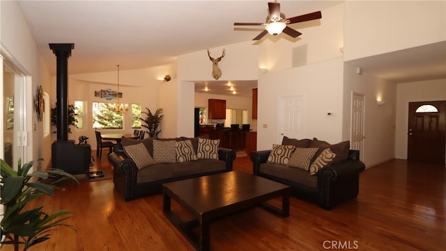 living room with ceiling fan with notable chandelier, dark wood-type flooring, a wood stove, and high vaulted ceiling