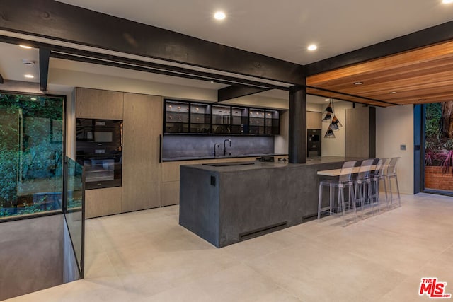 kitchen with double oven, a kitchen island, beam ceiling, a breakfast bar, and dark brown cabinetry