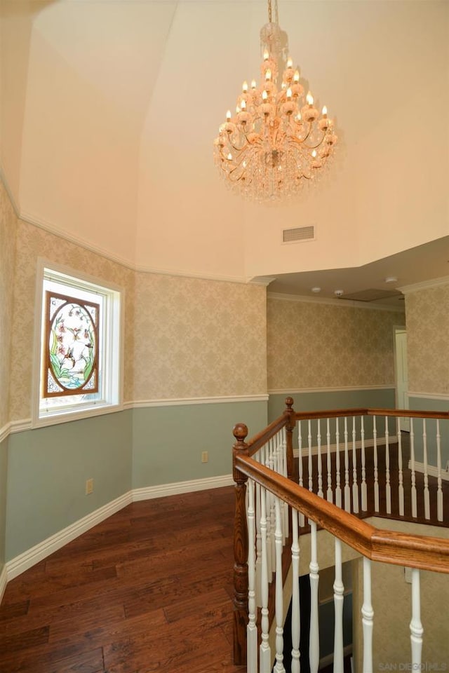 staircase with a notable chandelier, lofted ceiling, ornamental molding, and hardwood / wood-style flooring