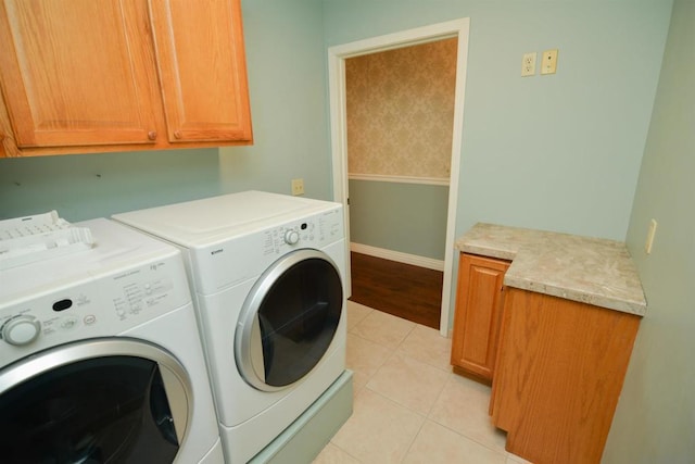 clothes washing area featuring cabinets, light tile patterned floors, and washing machine and dryer