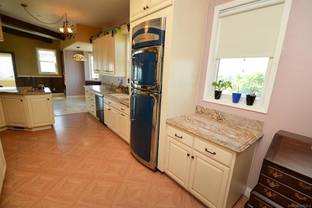 kitchen featuring sink, cream cabinets, decorative light fixtures, black dishwasher, and light stone countertops