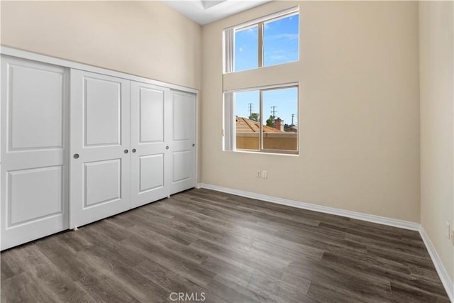 unfurnished bedroom with a closet, a high ceiling, and dark hardwood / wood-style floors