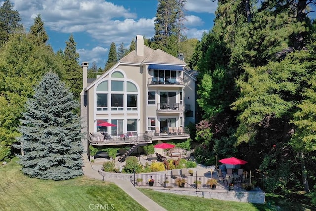 rear view of property with a yard, a balcony, and a patio