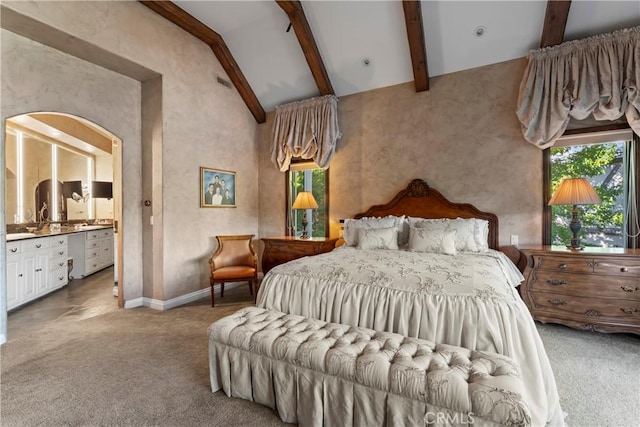 bedroom with high vaulted ceiling, light colored carpet, connected bathroom, and beam ceiling