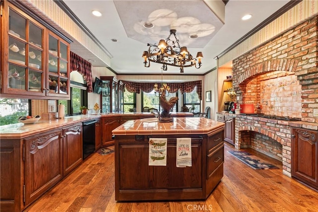 kitchen with dishwasher, light hardwood / wood-style floors, a kitchen island, a tray ceiling, and tile counters