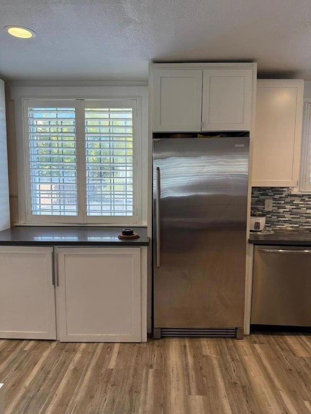 kitchen featuring a textured ceiling, white cabinets, appliances with stainless steel finishes, light hardwood / wood-style floors, and backsplash