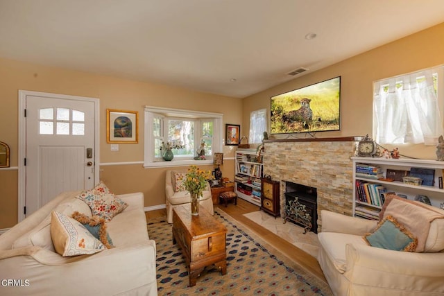 living room featuring plenty of natural light, light hardwood / wood-style flooring, and a stone fireplace