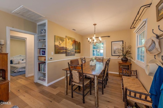 dining space with built in features, a chandelier, and light wood-type flooring