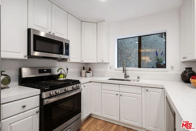 kitchen with white cabinets, sink, stainless steel appliances, and light hardwood / wood-style flooring