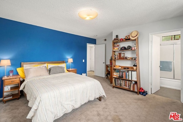 carpeted bedroom with ensuite bathroom and a textured ceiling