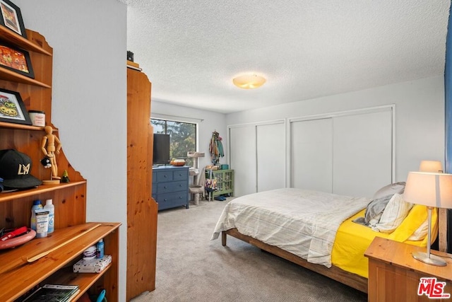 carpeted bedroom featuring a textured ceiling and multiple closets