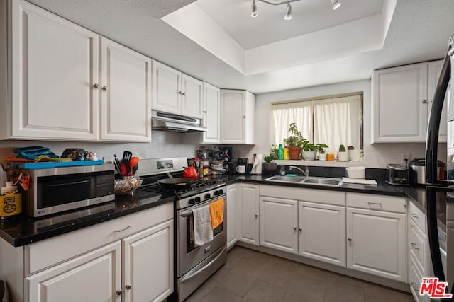 kitchen featuring appliances with stainless steel finishes, a raised ceiling, dark tile patterned floors, sink, and white cabinetry