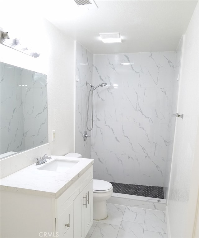 bathroom with a tile shower, vanity, and toilet