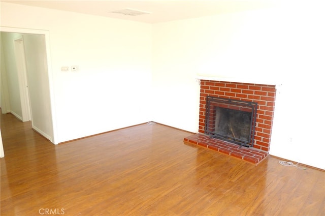 unfurnished living room featuring wood-type flooring and a brick fireplace