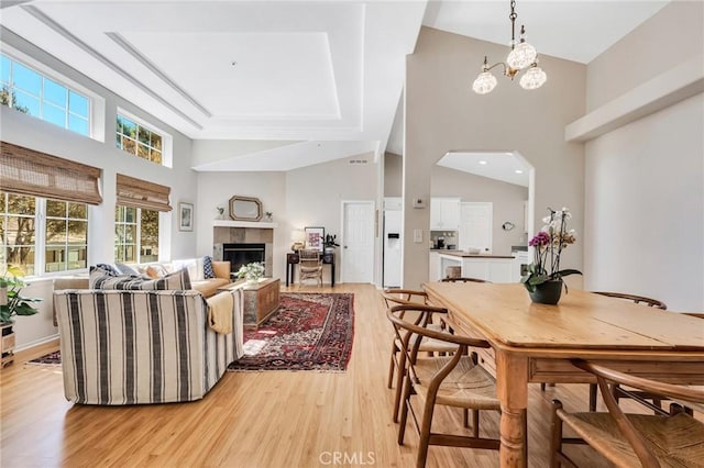 dining room featuring a chandelier, high vaulted ceiling, a tiled fireplace, and light wood-style floors