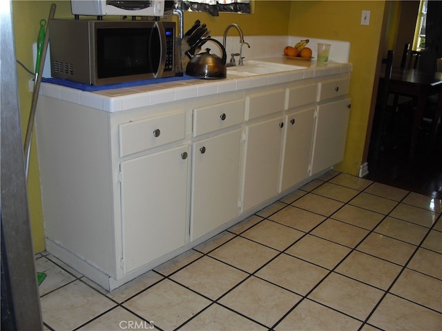 kitchen featuring white cabinetry, tile counters, light tile patterned floors, and sink