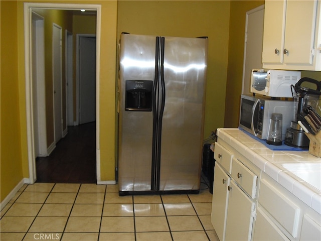 kitchen with light tile patterned flooring, stainless steel appliances, tile countertops, and white cabinetry