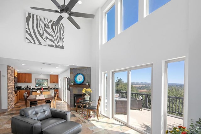 living room with ceiling fan, a towering ceiling, and a tile fireplace