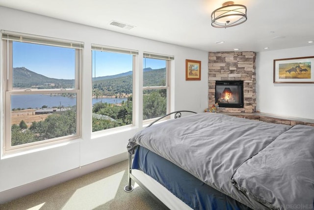 carpeted bedroom with a water and mountain view, multiple windows, and a fireplace