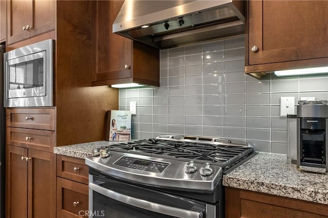 kitchen featuring appliances with stainless steel finishes, wall chimney exhaust hood, light stone countertops, and decorative backsplash