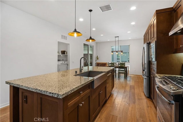 kitchen with hanging light fixtures, appliances with stainless steel finishes, a center island with sink, and washer and clothes dryer