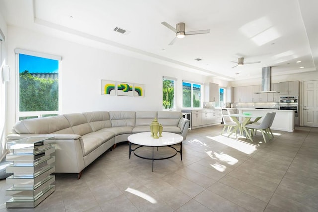 tiled living room featuring a raised ceiling and ceiling fan