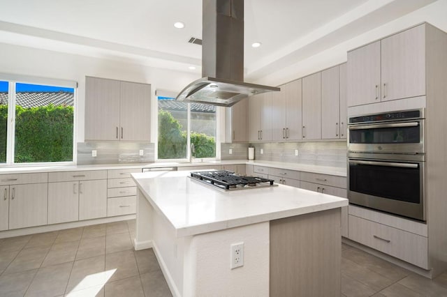 kitchen with light tile patterned floors, a kitchen island, island range hood, backsplash, and appliances with stainless steel finishes