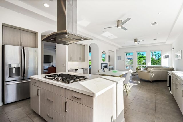 kitchen featuring dark tile patterned floors, a center island, island range hood, stainless steel appliances, and ceiling fan