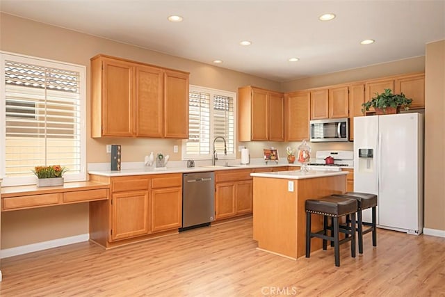 kitchen with sink, light hardwood / wood-style flooring, a kitchen breakfast bar, a kitchen island, and stainless steel appliances