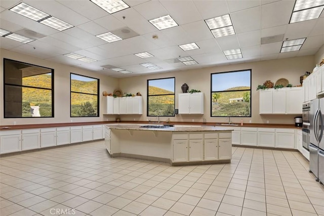 kitchen featuring a center island, a kitchen breakfast bar, stainless steel fridge, light tile patterned flooring, and white cabinetry