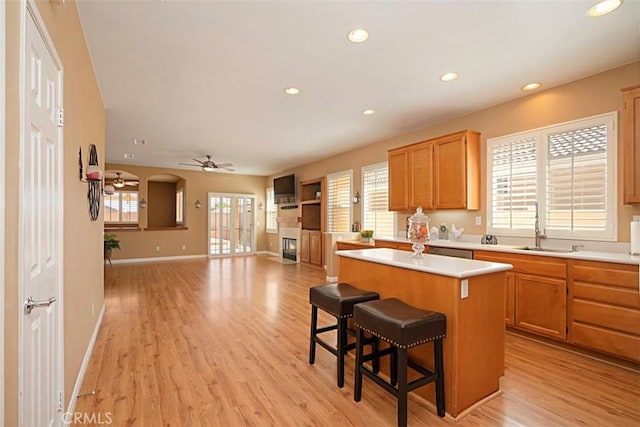 kitchen with a center island, a kitchen breakfast bar, sink, ceiling fan, and light wood-type flooring