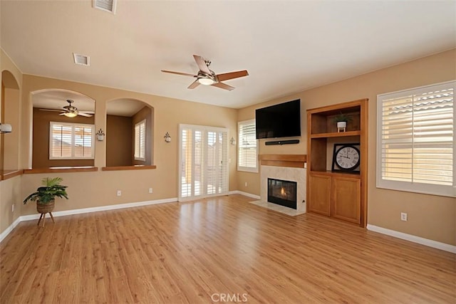 unfurnished living room with ceiling fan, built in features, a tile fireplace, and light hardwood / wood-style flooring