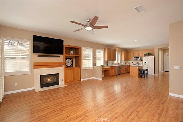 unfurnished living room featuring sink, light hardwood / wood-style flooring, ceiling fan, and a tiled fireplace