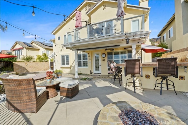 rear view of property with a balcony, an outdoor bar, and a patio area