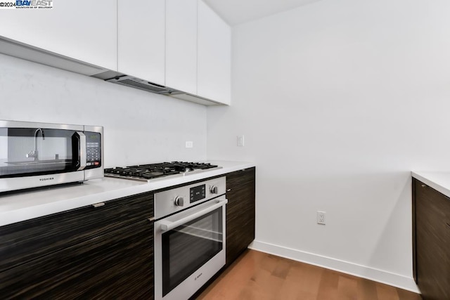 kitchen featuring white cabinets, dark brown cabinetry, hardwood / wood-style floors, and appliances with stainless steel finishes