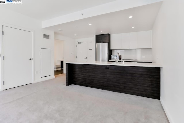 kitchen with stainless steel refrigerator, white cabinetry, dark brown cabinetry, and light carpet