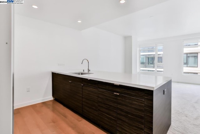 kitchen with kitchen peninsula, dark brown cabinetry, light hardwood / wood-style floors, and sink