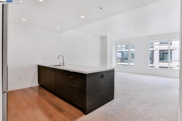 kitchen featuring kitchen peninsula, dark brown cabinetry, sink, and wood-type flooring