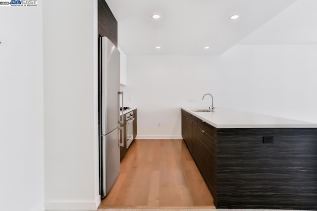 kitchen featuring stainless steel fridge, dark brown cabinets, light hardwood / wood-style flooring, and sink