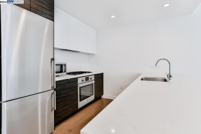 kitchen featuring appliances with stainless steel finishes, dark brown cabinetry, sink, hardwood / wood-style flooring, and white cabinets