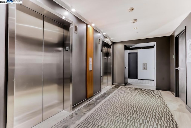 hall with light colored carpet and elevator